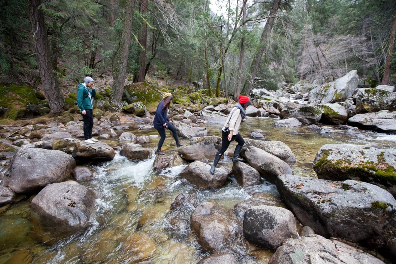 Three people stepping across a forest stream together